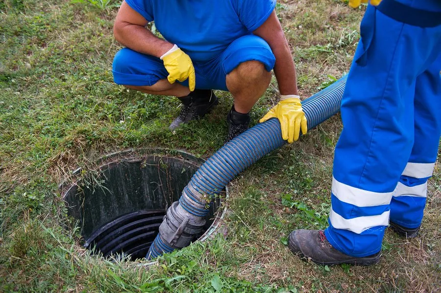 A pair of septic specialists monitoring a hose inside a tank